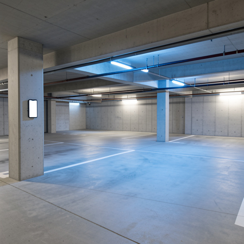Place de stationnement libre dans un parking résidentiel moderne, éclairée par une lumière bleutée, avec un smartphone posé sur un pilier.